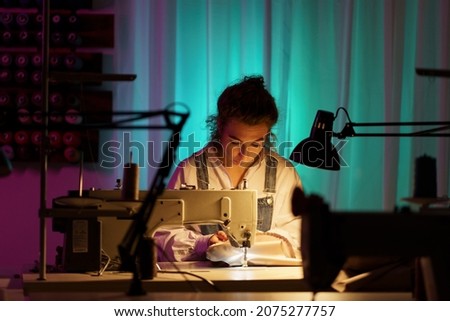 Tailor self-employment: young woman work on sewing machine in little creative atelier creating bespoke clothes for clients. Female learn modiste work for professional occupation. Tailoring business Royalty-Free Stock Photo #2075277757