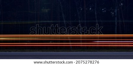 Car running lights in blurred motion on highway against dark blurred forest background Royalty-Free Stock Photo #2075278276
