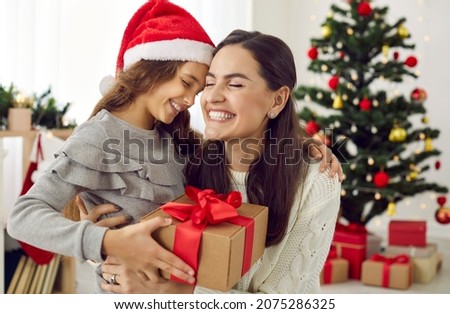 Happy family sharing joy with each other on Christmas. Mother receives gifts from her loving child on Xmas Day. Smiling daughter gives present to mommy in living room with decorated tree in background