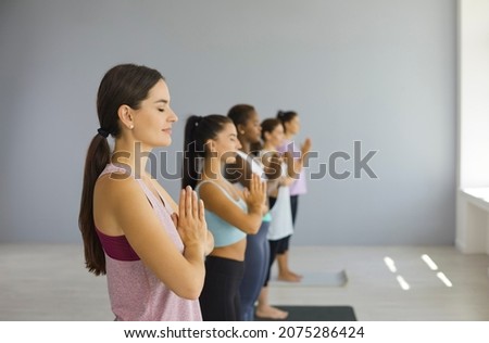 Find inner peace. Profile view of calm happy woman meditating with their eyes closed together with other women in yoga class. Practicing yoga in a bright studio. Selective focus. Blurred background.
