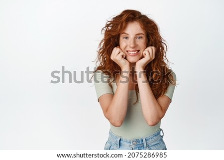 Beautiful redhead woman with natural long curly hair and freckles, clean face without makeup, smiling and gazing at camera, showing cute face, white background