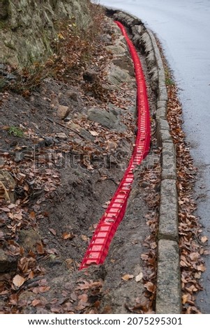 Communication Cables covered by red plastic flexible tube, Network Buildout high-speed Internet Network cables in red Cable Protector Wire Cover are buried underground on Construction site. 