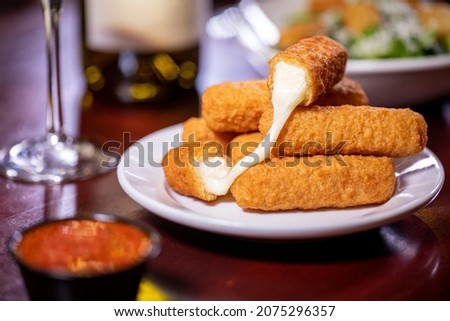 appetizer shareable starter small white saucer plate six deep-fried cheesy mozzarella sticks red pomodoro marinara dipping sauce rustic wooden dining table white wine glass bottle side dishes Royalty-Free Stock Photo #2075296357