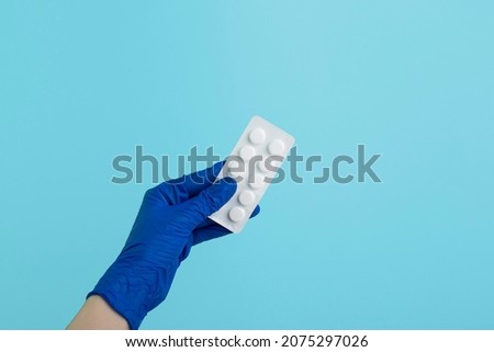 Small pill in the hand in medical gloved palm on blue background. Stop corona virus. Don't panic. 