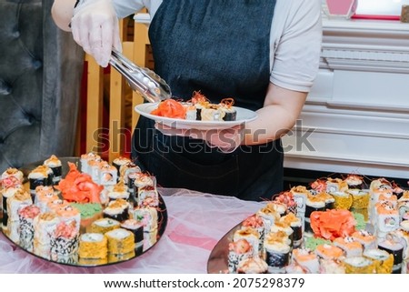 The waiter puts sushi on the plate. Sushi and sushi roll set, sushi rolls served with wasabi and ginger