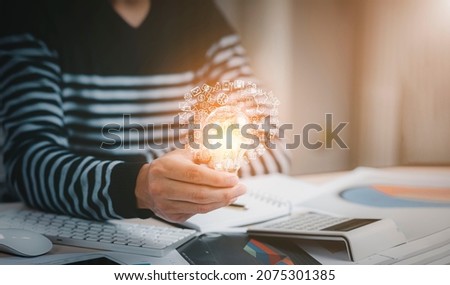 Creativity and innovation are keys success concept, businessman hand holding light bulb with using calculator to calculate and money stack. idea saving energy and accounting finance in office concept