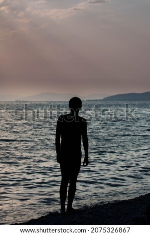 Contemporary art dramatic portrait silhouette a man at the sea in rays of the setting sun against the backdrop dark waves and beautiful evening sky