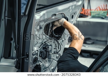 Auto service worker disassembles car door for repair, restoration, tuning car sound or installing noise insulation or soundproofing Royalty-Free Stock Photo #2075328343