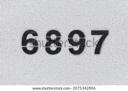 Black Number 6897 on the white wall. Spray paint. Number six thousand eight hundred and ninety seven.