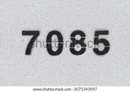 Black Number 7085 on the white wall. Spray paint. Number seven thousand eighty five.