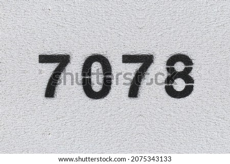 Black Number 7078 on the white wall. Spray paint. Number seven thousand seventy eight.