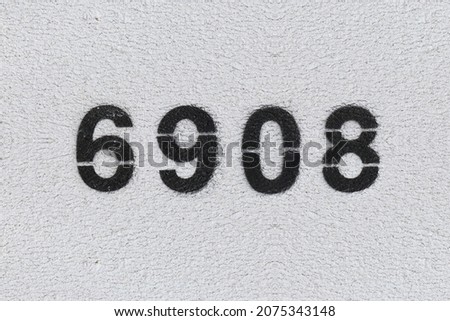 Black Number 6908 on the white wall. Spray paint. Number six thousand nine hundred and eight.