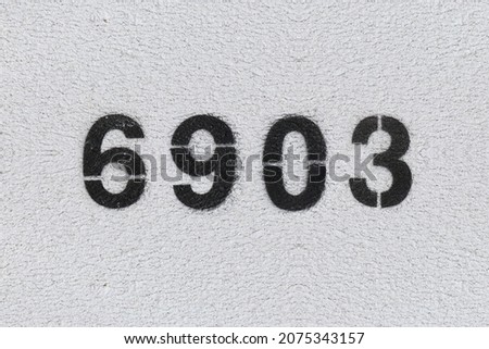 Black Number 6903 on the white wall. Spray paint. Number six thousand nine hundred three.