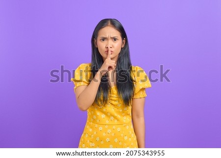 Portrait of attractive young Asian woman making silence gesture on purple background