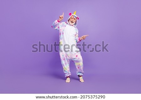 Photo of funny excited man pensioner unicorn sleepwear pointing fingers empty space dancing smiling isolated violet color background