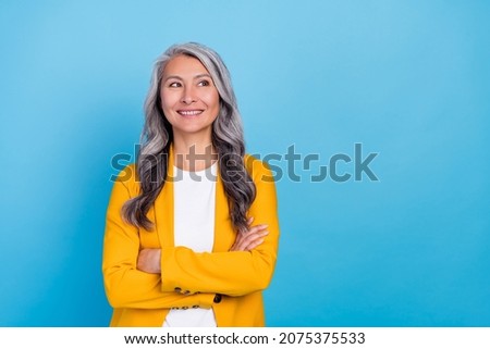 Photo of dreamy charming senior lady dressed yellow blazer arms folded looking empty space smiling isolated blue color background