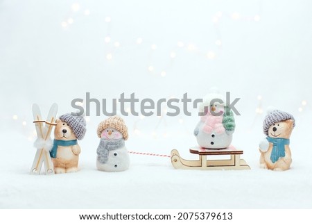 Decorative Christmas-themed figurines. The statuette of a cat, penguin and a bear with ski and a snoman on the sledge. Cute animals in a knitted hat on the white background. Warm bokeh lights