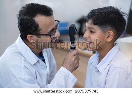 Optometrist is examining the eyes of an Indian boy, ophthalmologist uses special device to examine the boy's vision Royalty-Free Stock Photo #2075379943