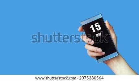 may 15. 15th day of the month, calendar date. Woman's hand holds mobile phone with blank screen on blue isolated background. Spring month, day of the year concept.