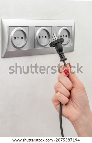 Hand holding plug near socket. Royalty-Free Stock Photo #2075387194