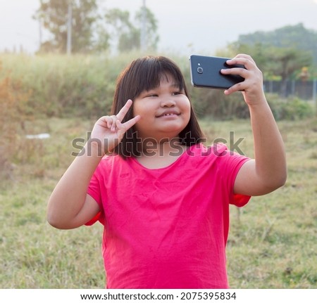 Happy portrait fat chubby girl Asian woman thailand be happy cute cheeks with black hair wearing red-pink shirt. Taking a picture with smartphone with a bright smile In evening at sunset front garden