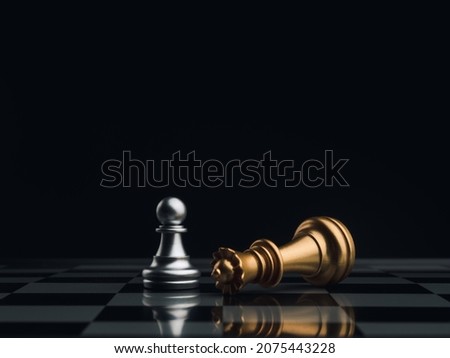 A little silver pawn chess piece standing with the win near a fallen golden queen chess piece on a chessboard on dark background. Leadership, winner, brave, competition, and business strategy concept. Royalty-Free Stock Photo #2075443228