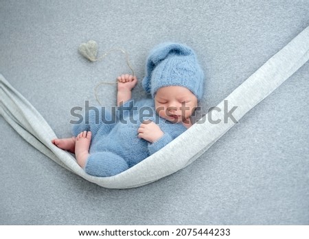 Newborn baby boy sleeping with knitted heart toy during studio photoshoot. Adorable infant child kid sleeping wearing hat and costume Royalty-Free Stock Photo #2075444233