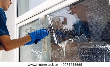 An employee of a professional cleaning service in overalls washes the glass of the windows of the facade of the building. Showcase cleaning for shops and businesses Royalty-Free Stock Photo #2075456665