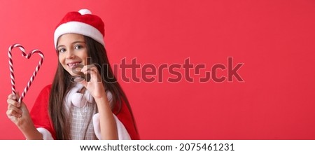 Cute little girl in Santa hat and with candy canes on red background with space for text