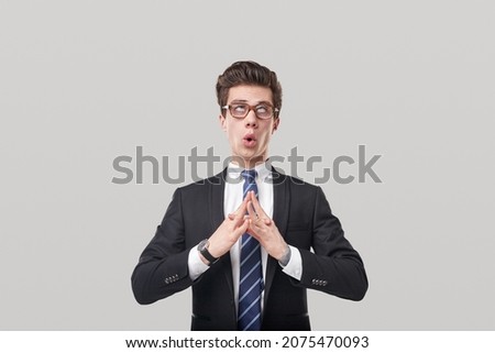 Comic tired male entrepreneur in suit breathing and doing yoga during hard working day on gray background in studio