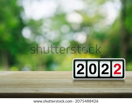 Retro flip clock with 2022 text on wooden table over blur green tree in park, Happy new year 2022 cover concept