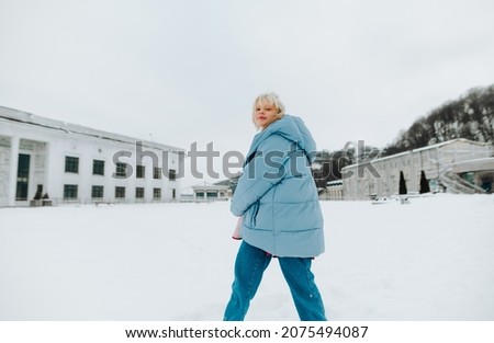 Beautiful girl in winter clothes spins on a snowy street and smiles looking at the camera.