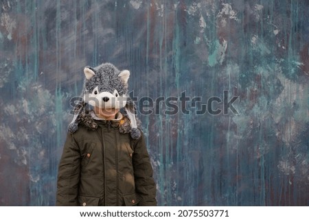 The child hiding behind a wolf's hat on gray background, outdoor. space for text. High quality photo