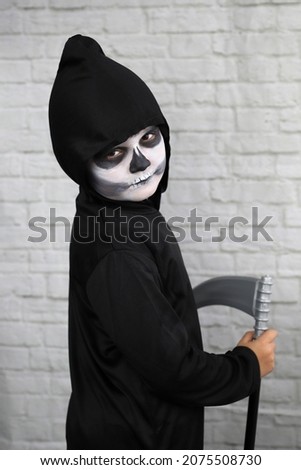child with a costume of the grim reaper with a scythe and with a make-up face
