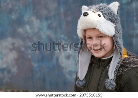 Portrait child in a wolf hat and smiles sweetly on gray background, outdoor. space for text. High quality photo