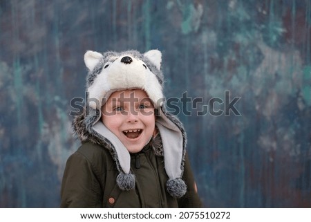 Portrait of a surprised child in a wolf hat and smiles sweetly on gray background, looking at the camera, outdoor. space for text. High quality photo