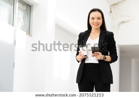 Portrait Of Successful A middle-aged Asian businesswoman Holding smart phone and coffee smiling to camera