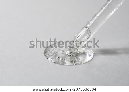 Transparent facial serum in glass pipette pouring on grey background. Drop of liquid gel with hyaluronic acid closeup. Cosmetic product macro. Copy space. Royalty-Free Stock Photo #2075536384