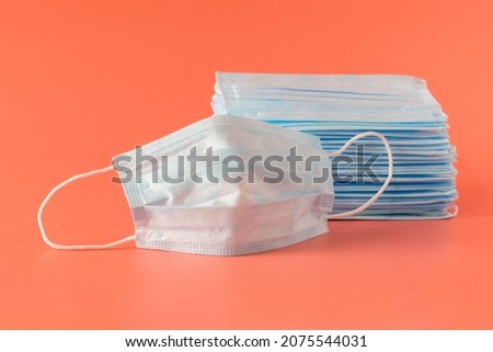 Many new medical facial three-layer masks are stacked and one mask lies next to it on a pink background