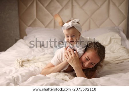 Cute blonde baby is having fun playing with her mom riding her mom. A white bed. motherhood. breastfeeding. High-quality photography