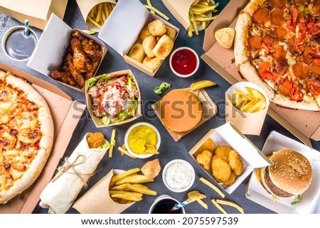 Delivery fastfood ordering food online concept. Large set of assorted take out foods pizza, french fries, fried chicken nuggets, burgers, salads, chicken wings, sides, black concrete background Royalty-Free Stock Photo #2075597539