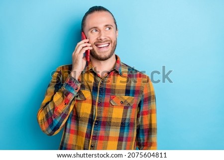 Photo of impressed young tail hairstyle guy talk telephone look empty space wear plaid shirt isolated on blue color background