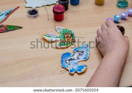 The artist draws on dry fallen leaves. Funny drawings of a bear cub and a horse. Acrylic paint and gouache. Adult woman. Indoors. Selective focus.