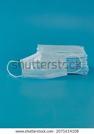 Many new medical surgical facial three-layer masks are stacked high and one mask lies next to the blue background. Copy Space