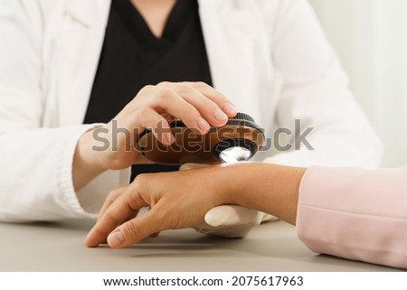 Doctor and client woman in dermatology clinic. Dermatologist is using dermatoscope for skin examination. Royalty-Free Stock Photo #2075617963