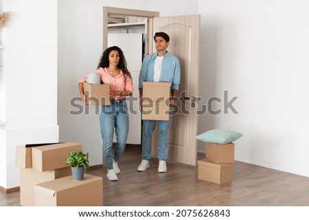 Unhappy confused millennial couple homeowners holding cardboard boxes walking in new house, young family of two people moving into bad flat, sad guy and lady disappointed in interior design