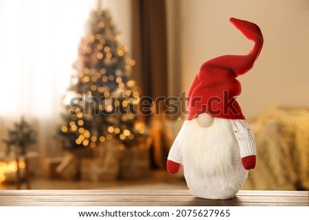 Funny Christmas gnome on wooden table in room with festive decorations. Space for text