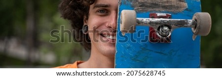 joyful young man obscuring face with skateboard while looking at camera, banner