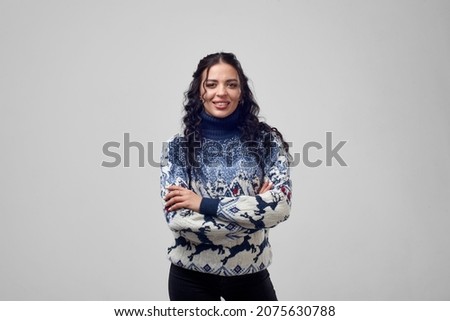 A young girl stands with her arms crossed in a New Year's sweater on a white background and smiles. Space for text.