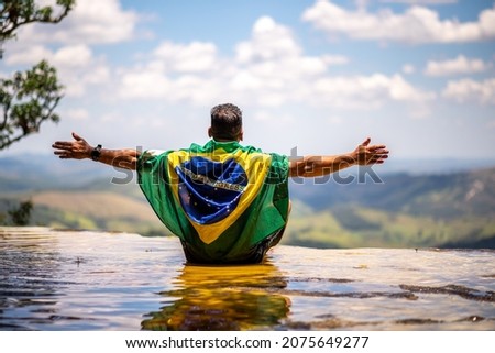 Man with Brazilian flag looking at the horizon. Top of Janela do Ceu Waterfall in Parque Estadual do Ibitipoca (Ibitipoca State Park), Minas Gerais, Brazil Royalty-Free Stock Photo #2075649277